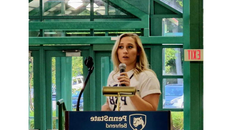 A person st和s at a podium giving a speech, the podium has a banner that reads Penn State Behrend